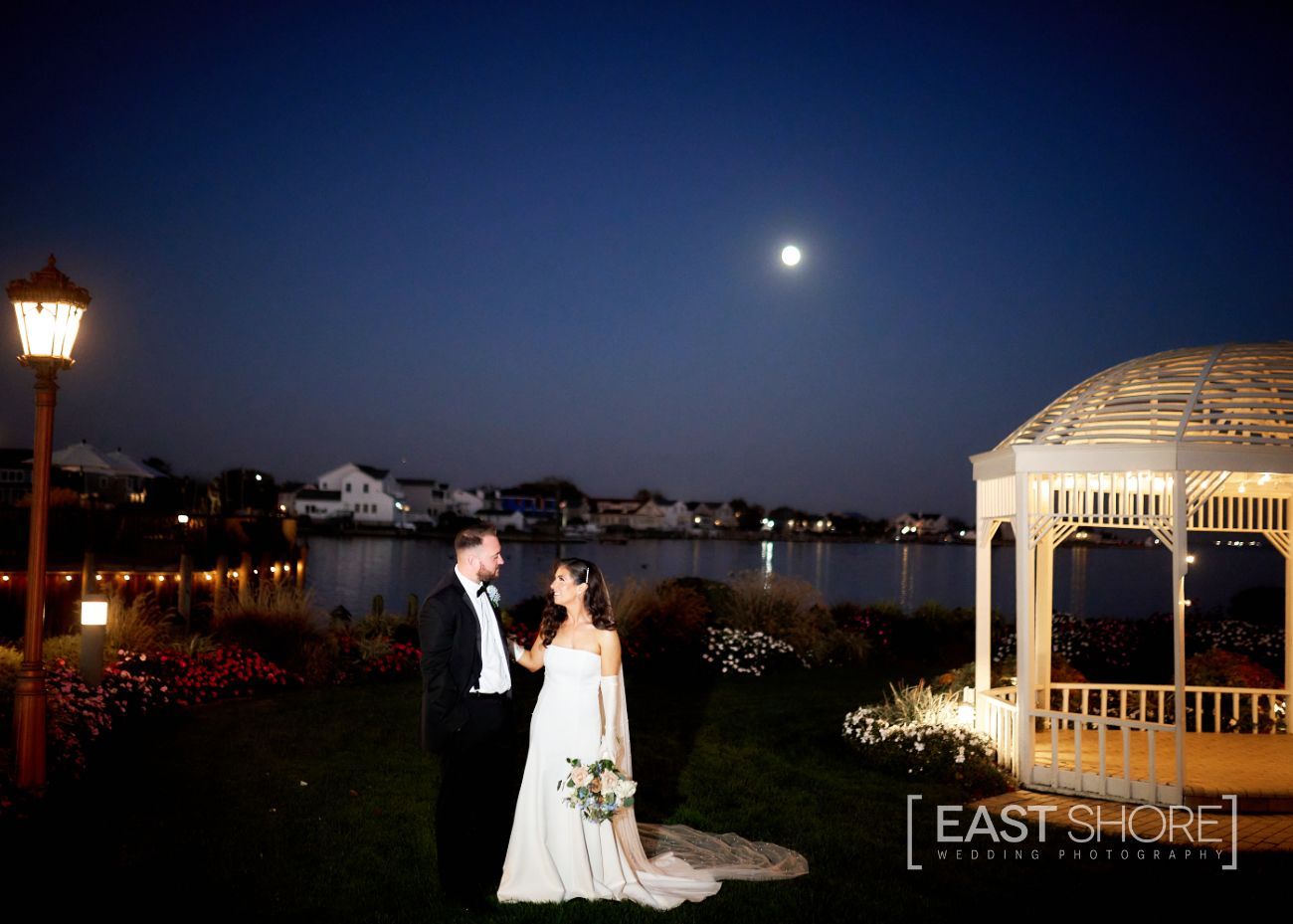 A bride and groom are standing in front of a gazebo at night.