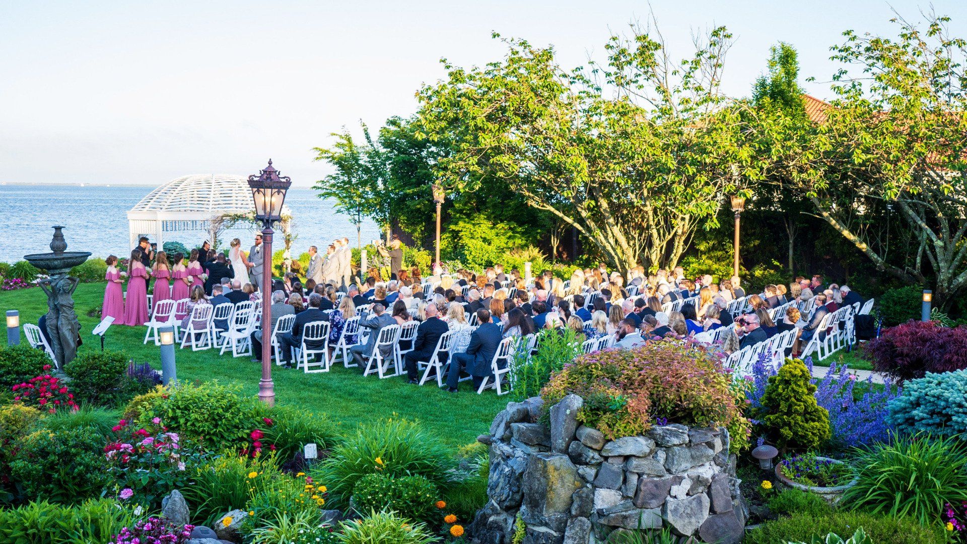 A large group of people are sitting in the grass at a wedding ceremony.