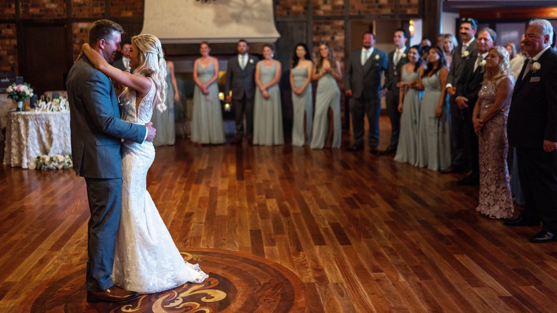 A bride and groom are dancing on a wooden floor in front of their wedding party.