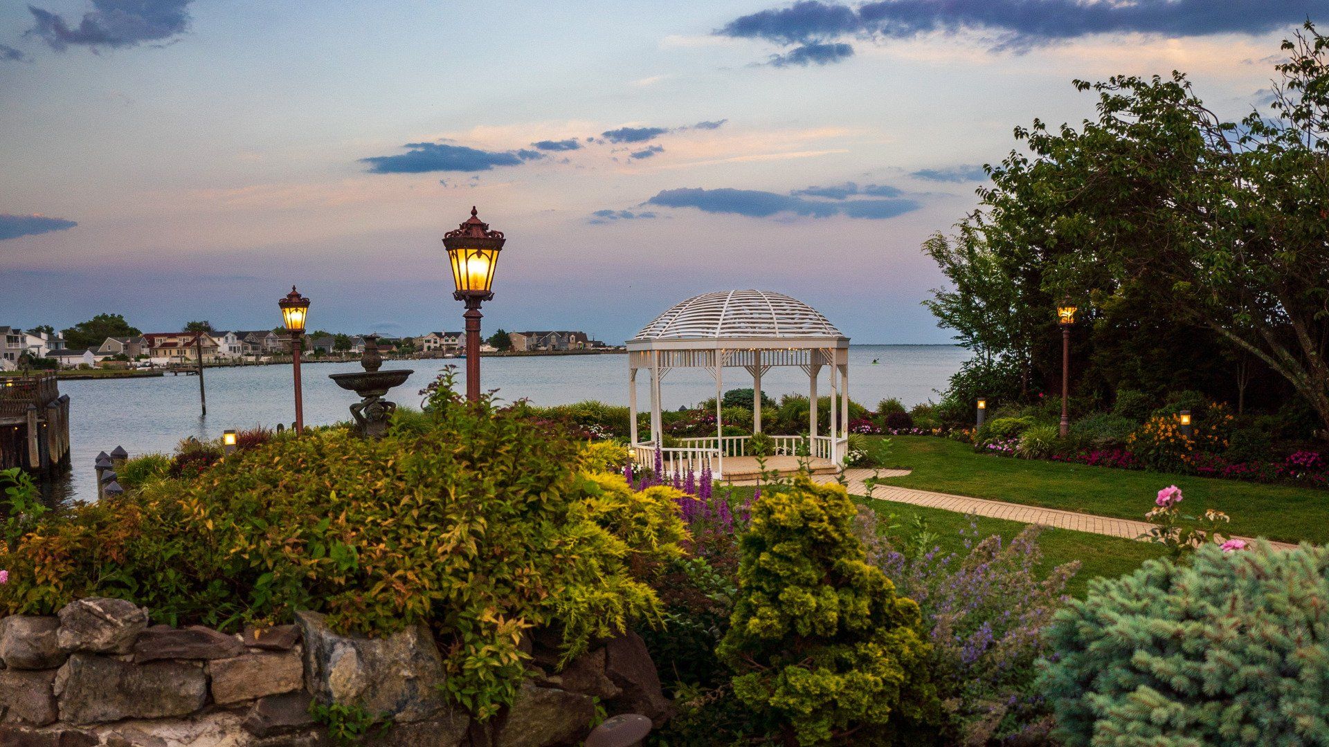 There is a gazebo in the middle of a garden overlooking the water.