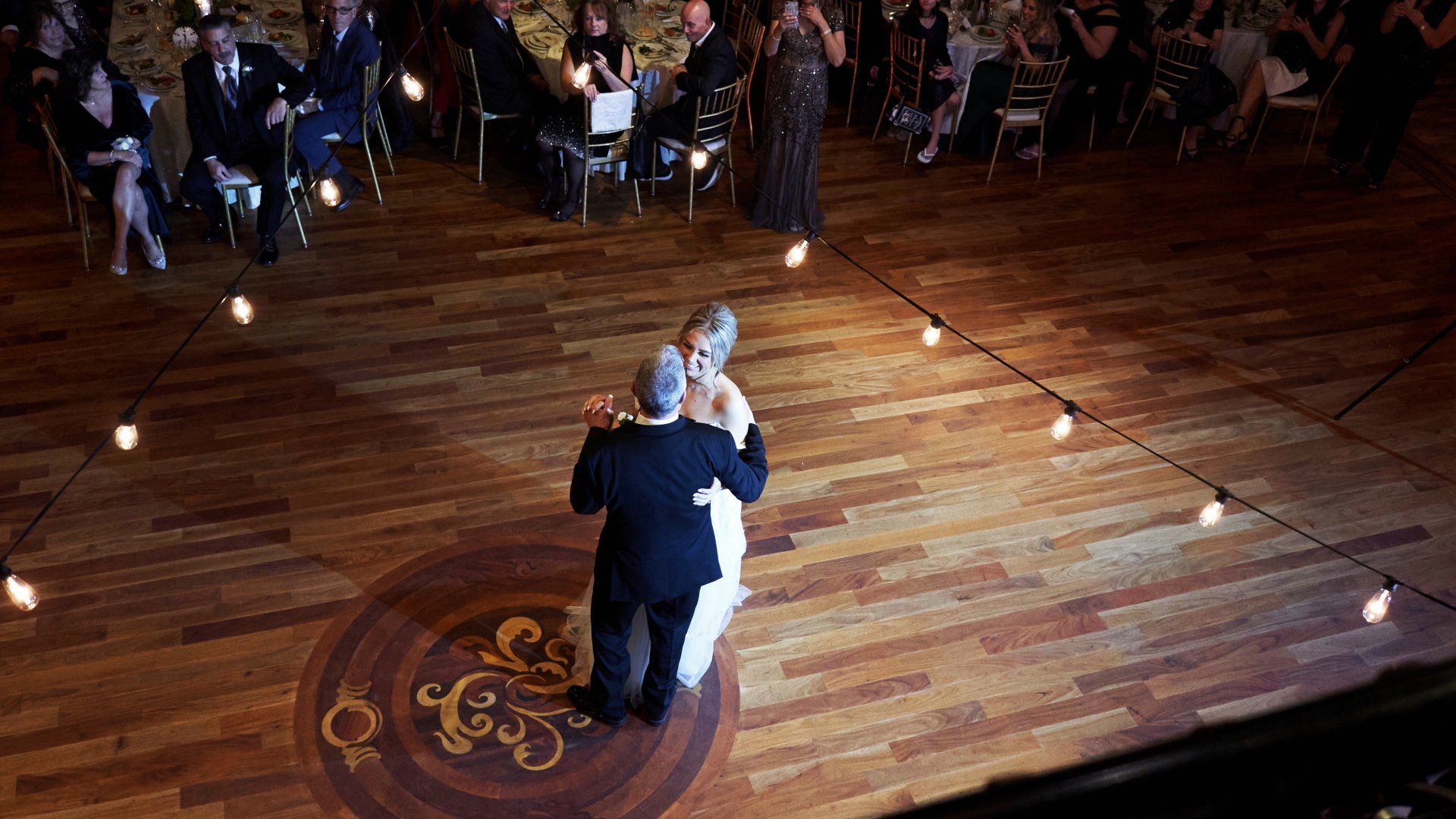 A bride and groom are dancing on a wooden dance floor at their wedding reception.