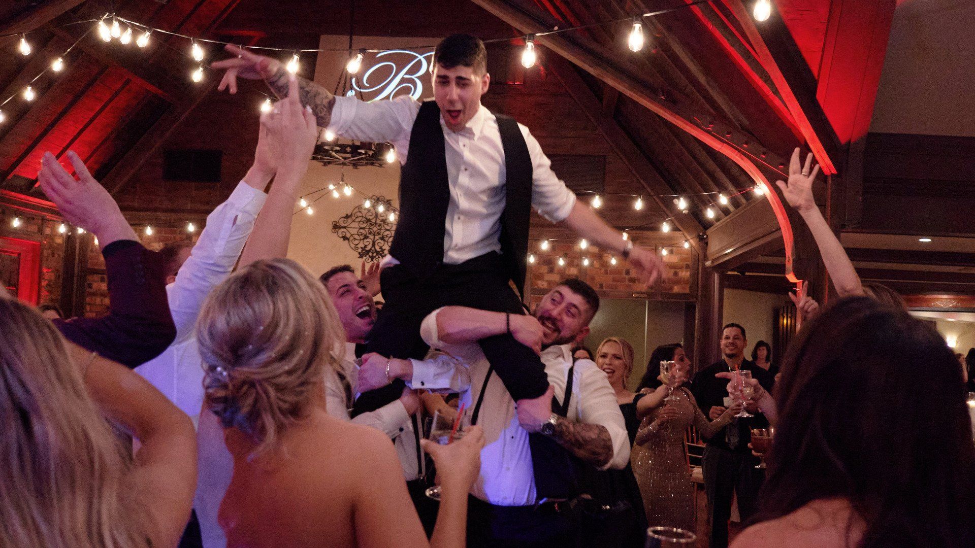 A man is being lifted in the air by a group of people at a wedding reception.
