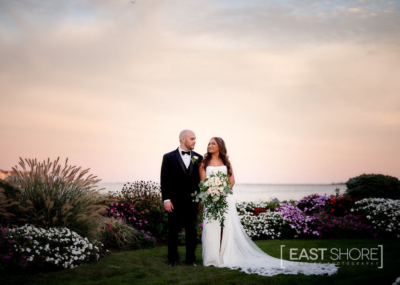 A bride and groom are posing for a picture in front of the ocean.