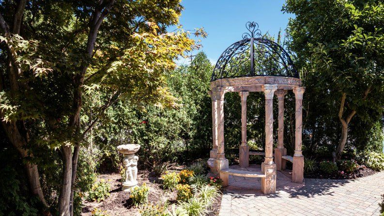 There is a gazebo in the middle of a garden surrounded by trees.
