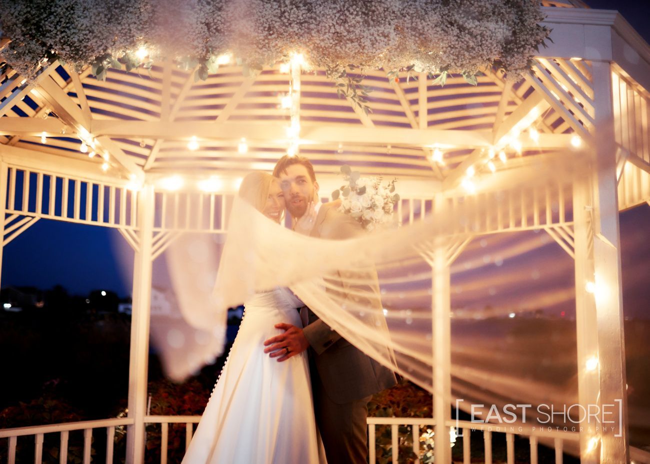 A bride and groom pose under a gazebo at night