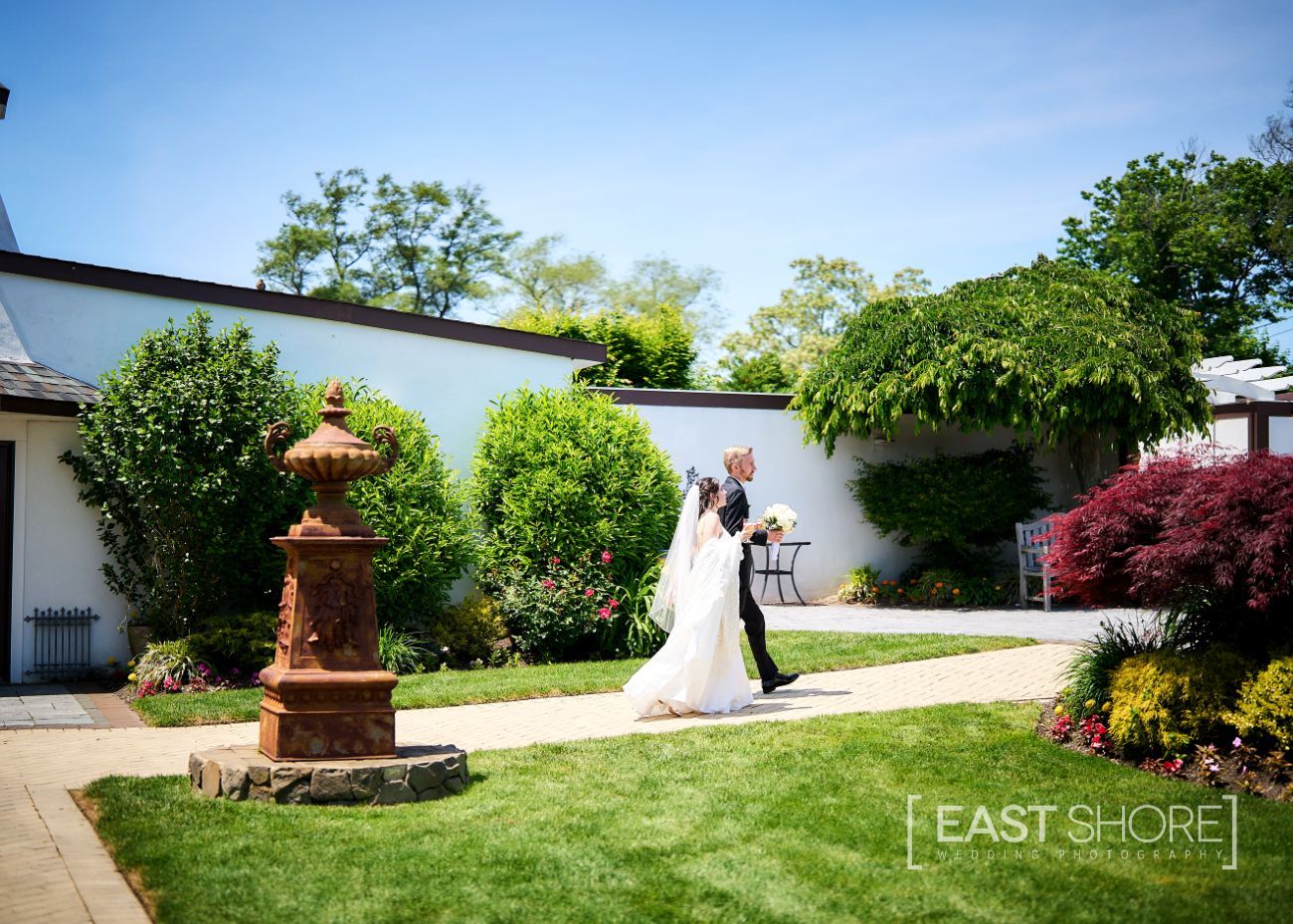 A bride and groom are walking down a path in a garden.