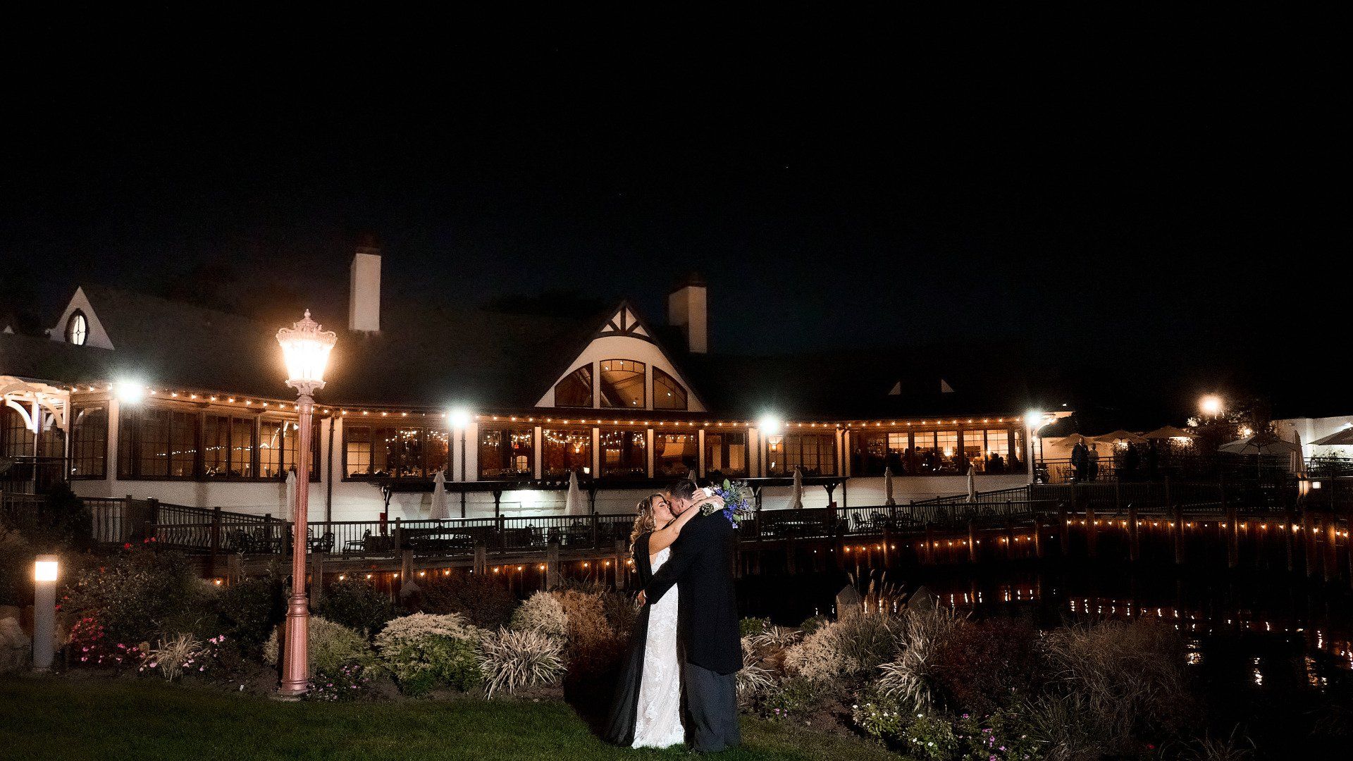 A bride and groom are kissing in front of a large building at night.
