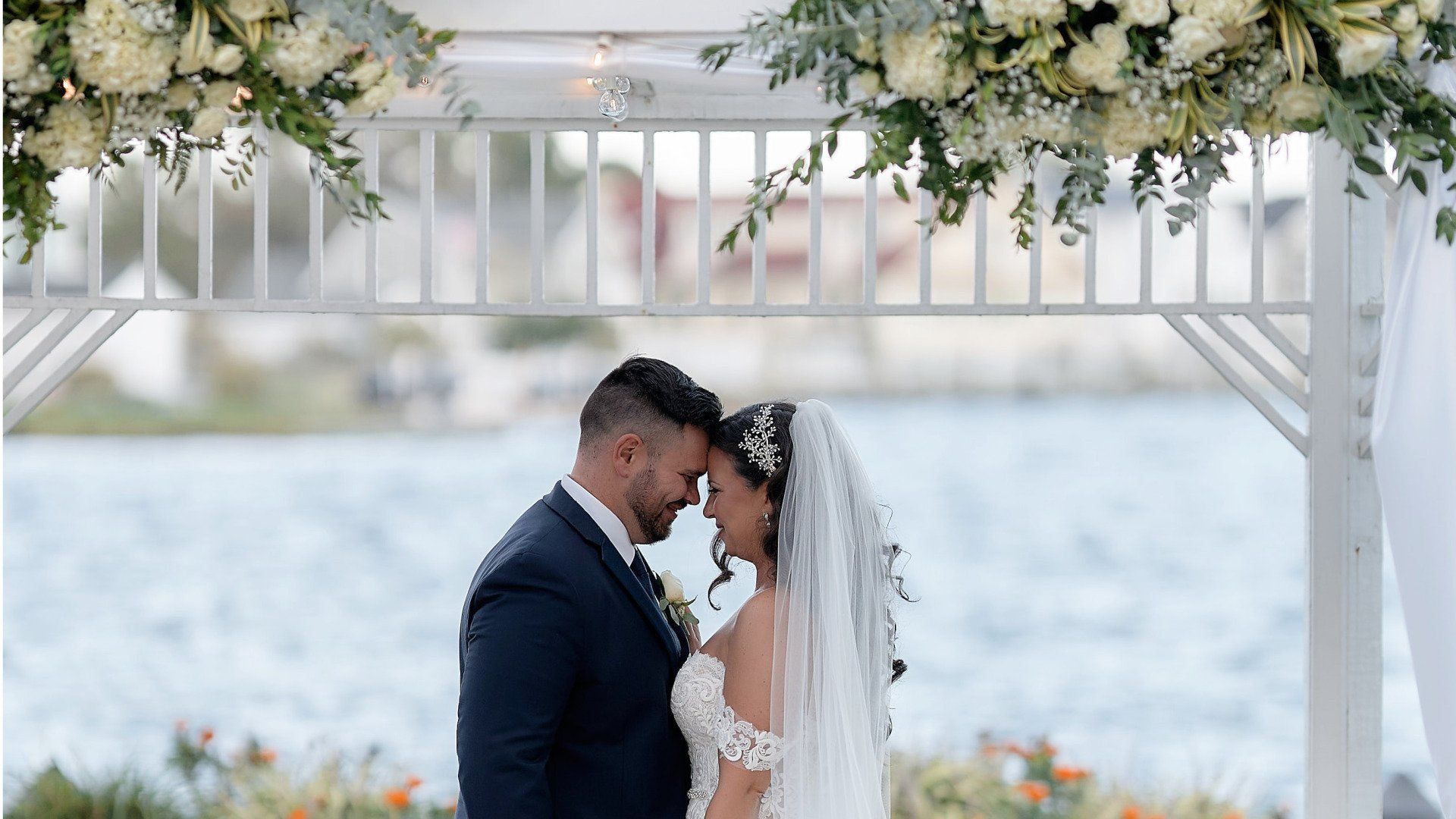 A bride and groom are standing under a gazebo overlooking a body of water.
