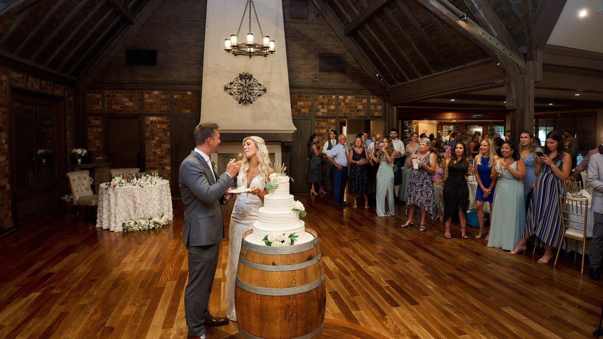 A bride and groom are cutting their wedding cake in front of their wedding guests.