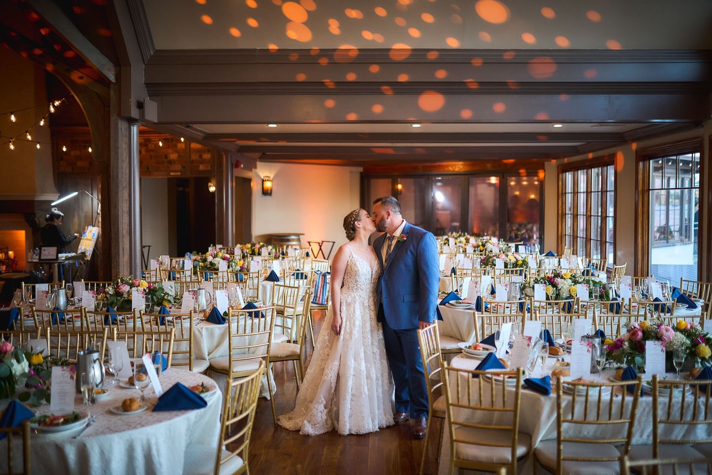 a bride and groom are kissing in a large room filled with tables and chairs .