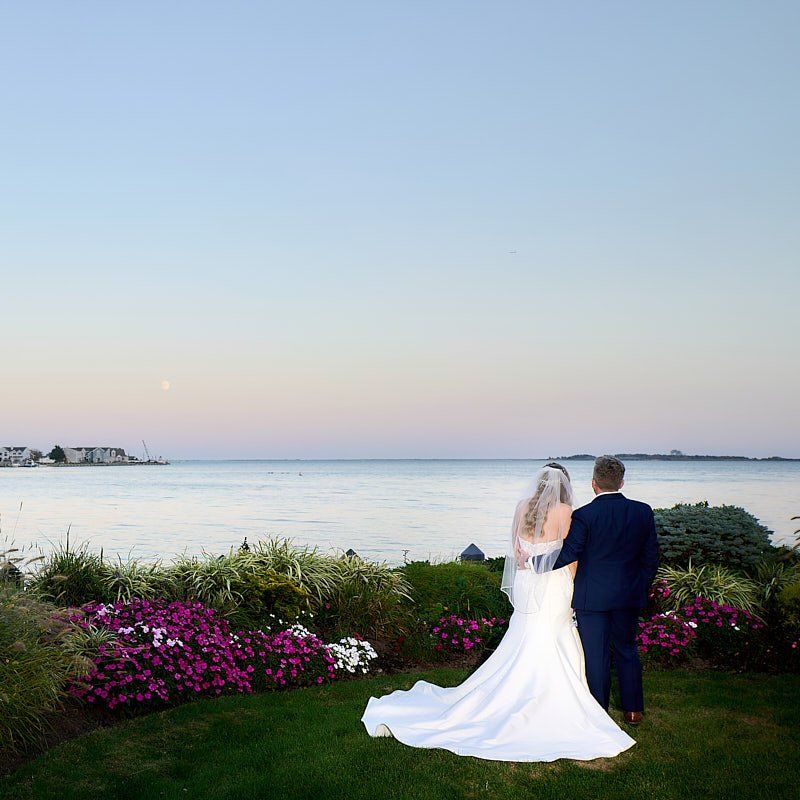A bride and groom standing in front of a body of water