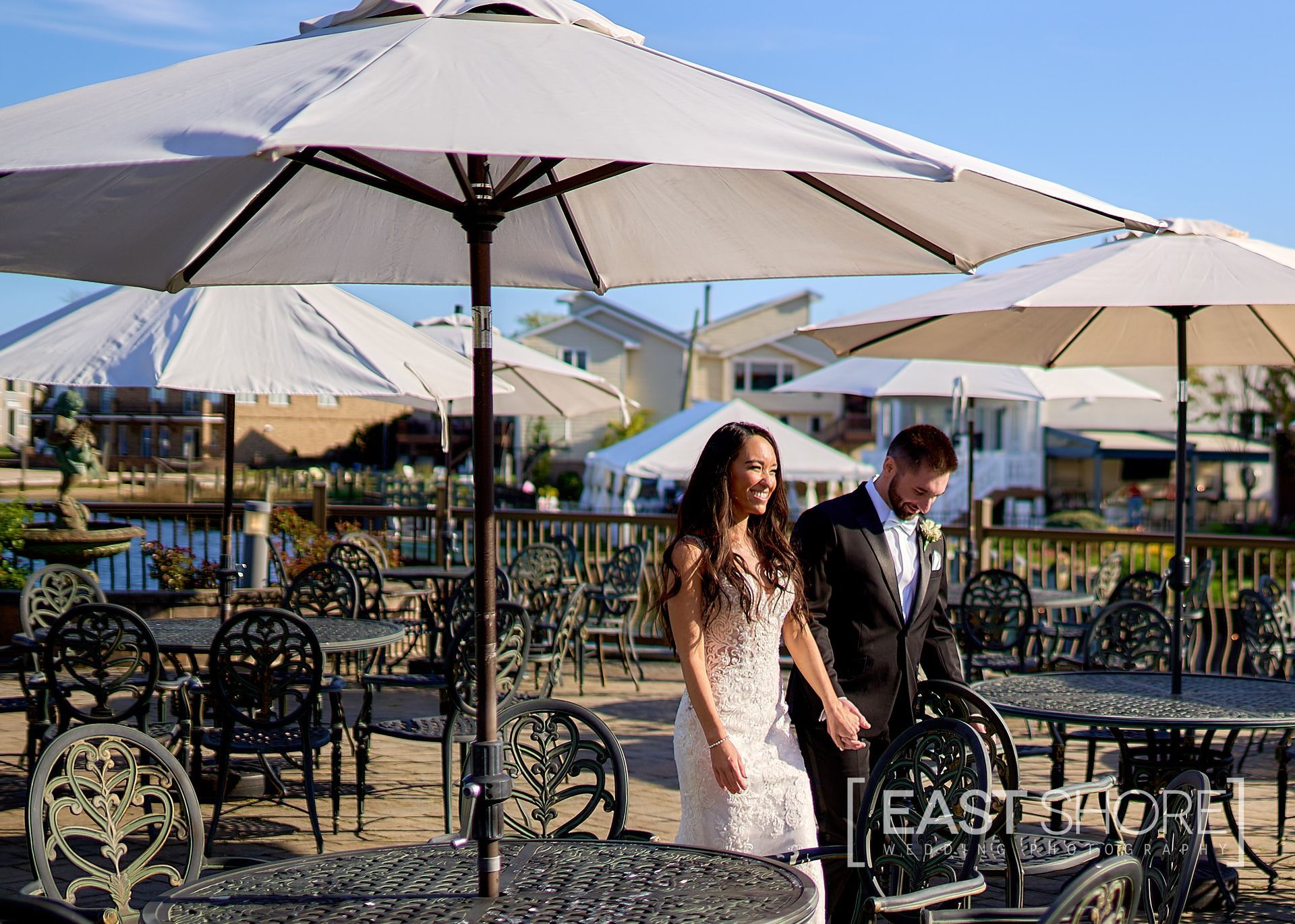 A bride and groom are standing under umbrellas at a restaurant.