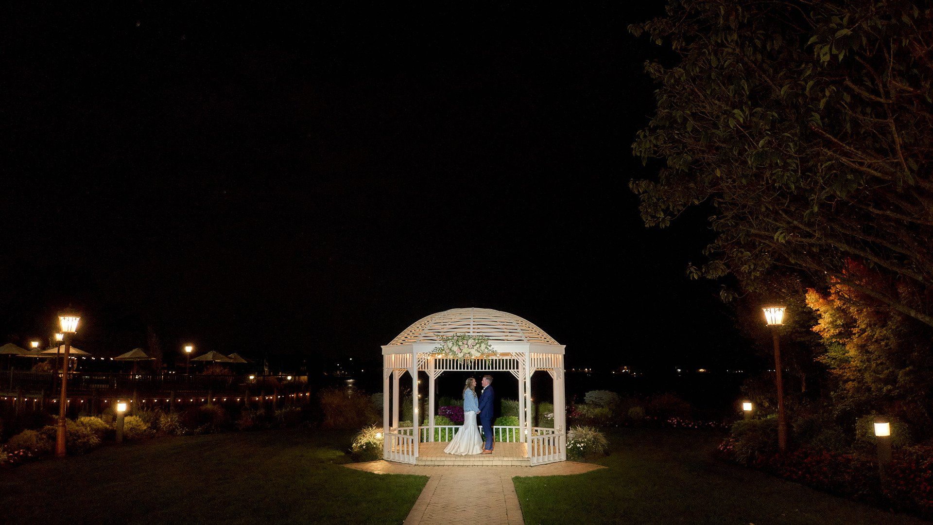A bride and groom are standing under a gazebo at night.