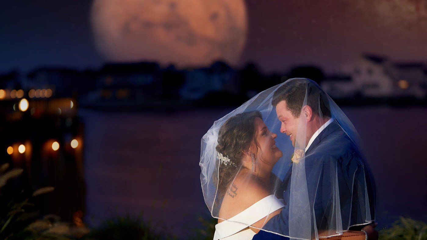 A bride and groom are posing for a picture in front of a full moon.
