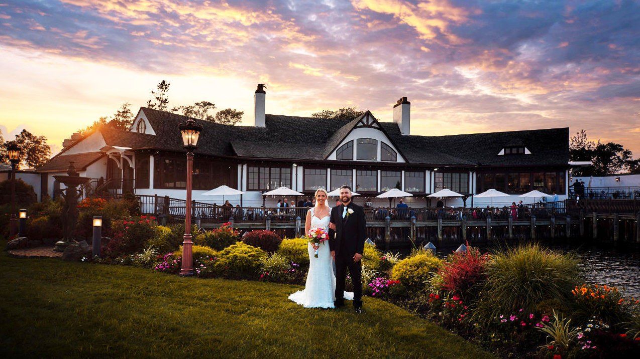 a bride and groom are standing in front of a large house at sunset .