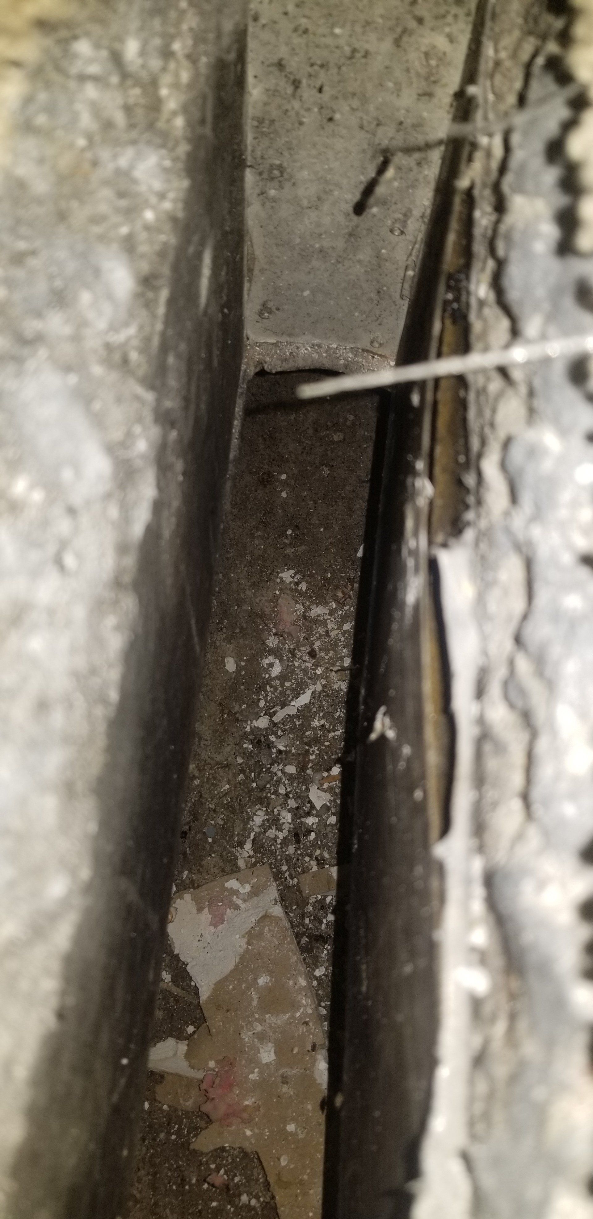 Close-up of a dark, narrow space between concrete walls, with a thin object inserted.