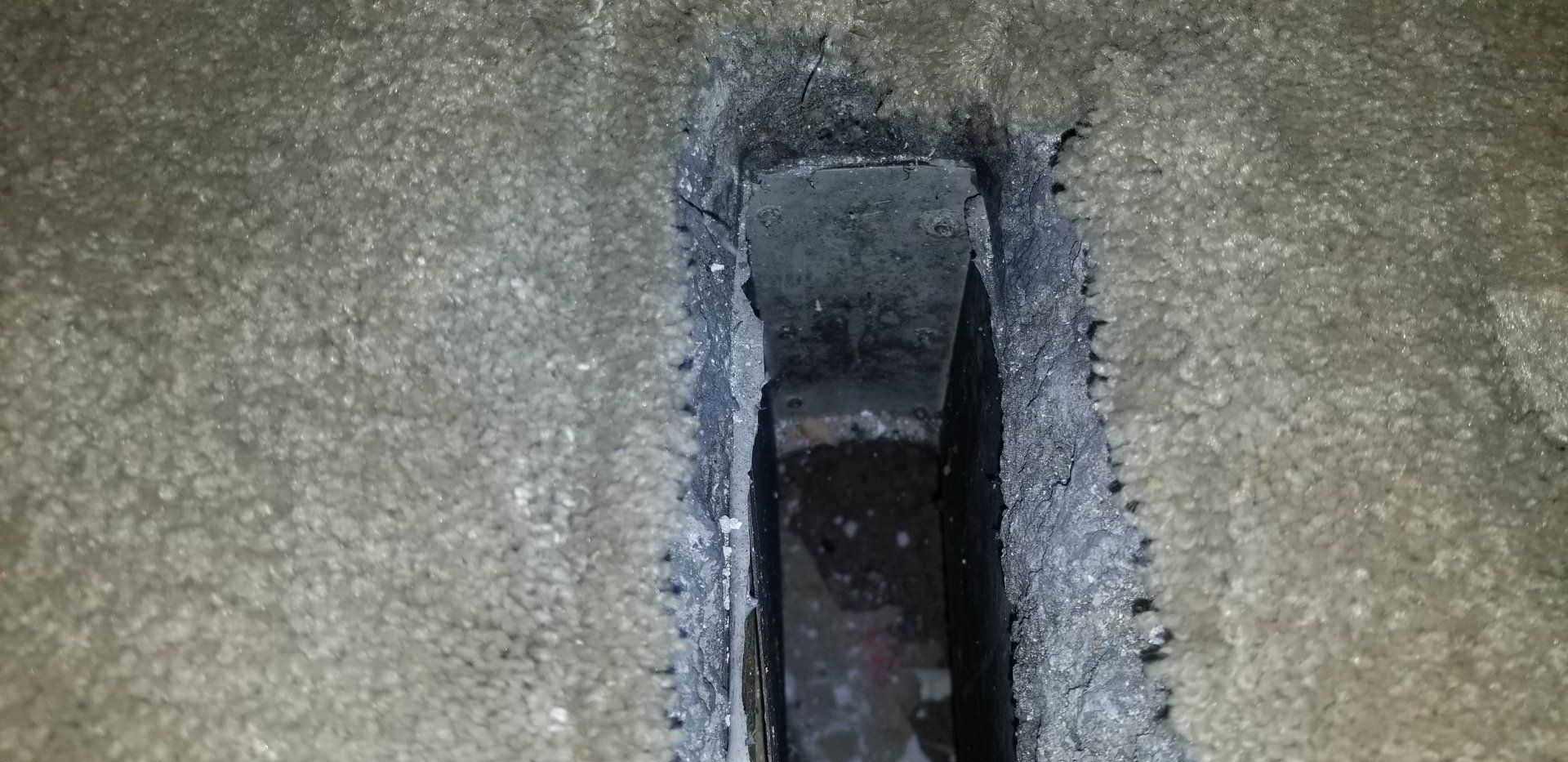 A narrow, dark trench in concrete, with a glimpse of an interior.