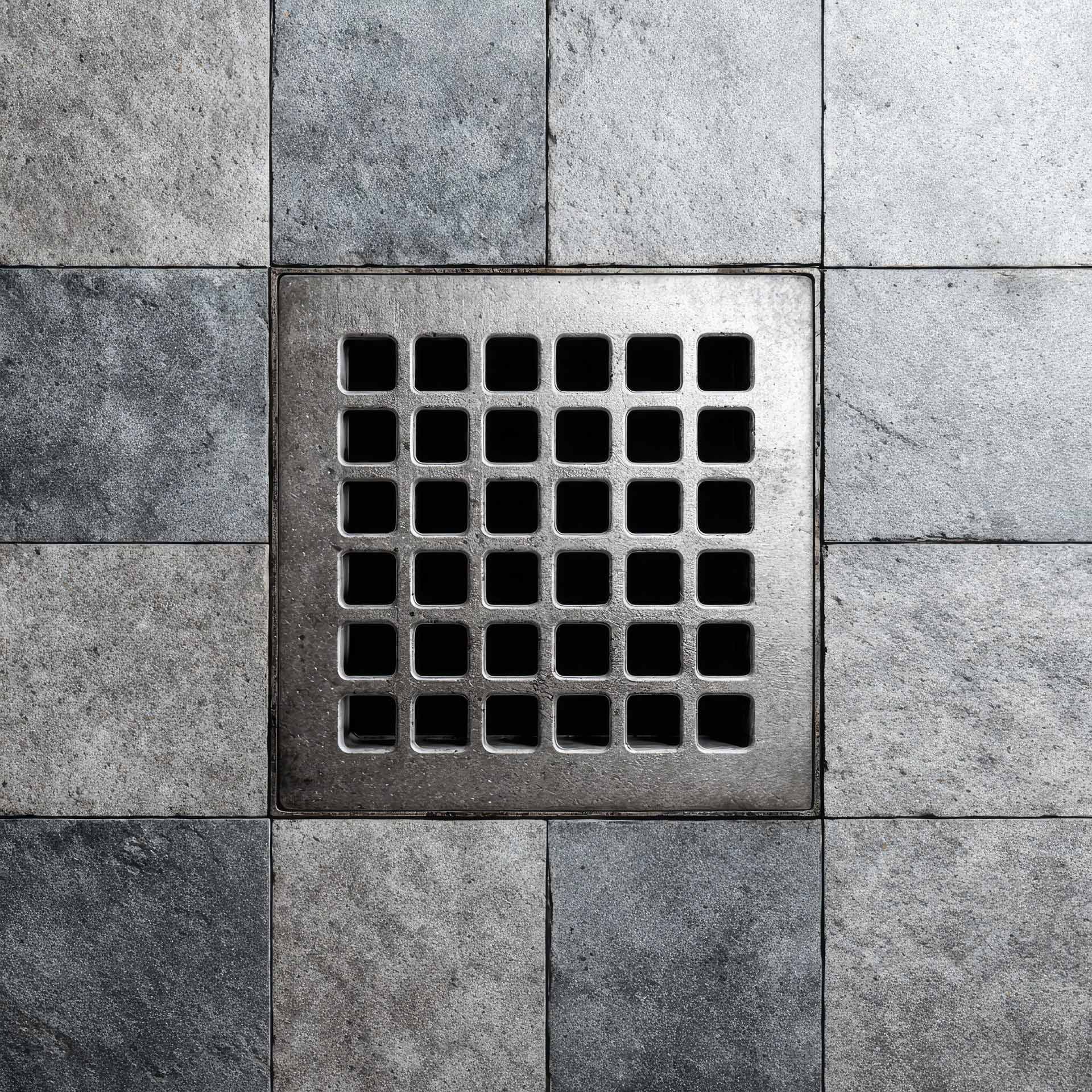 Metal drain grate on checkered tile floor.