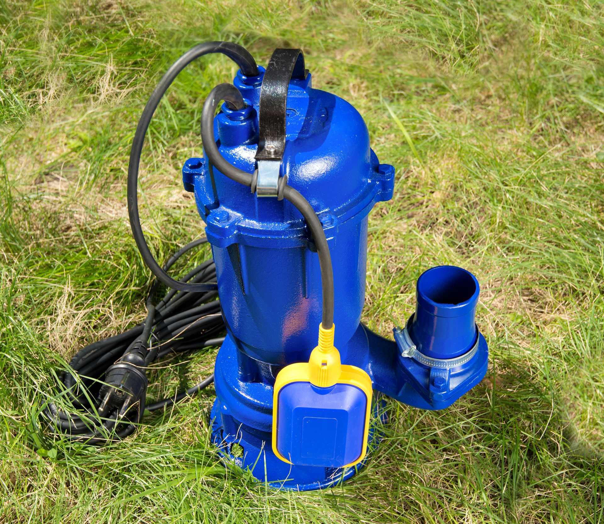 Blue submersible water pump with attached cables and float switch placed on green grass.