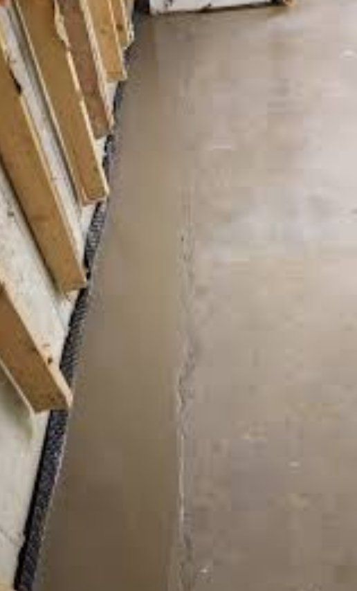 Water pooling along a concrete floor next to a wooden wall section.