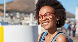 A woman wearing glasses and a backpack is smiling.
