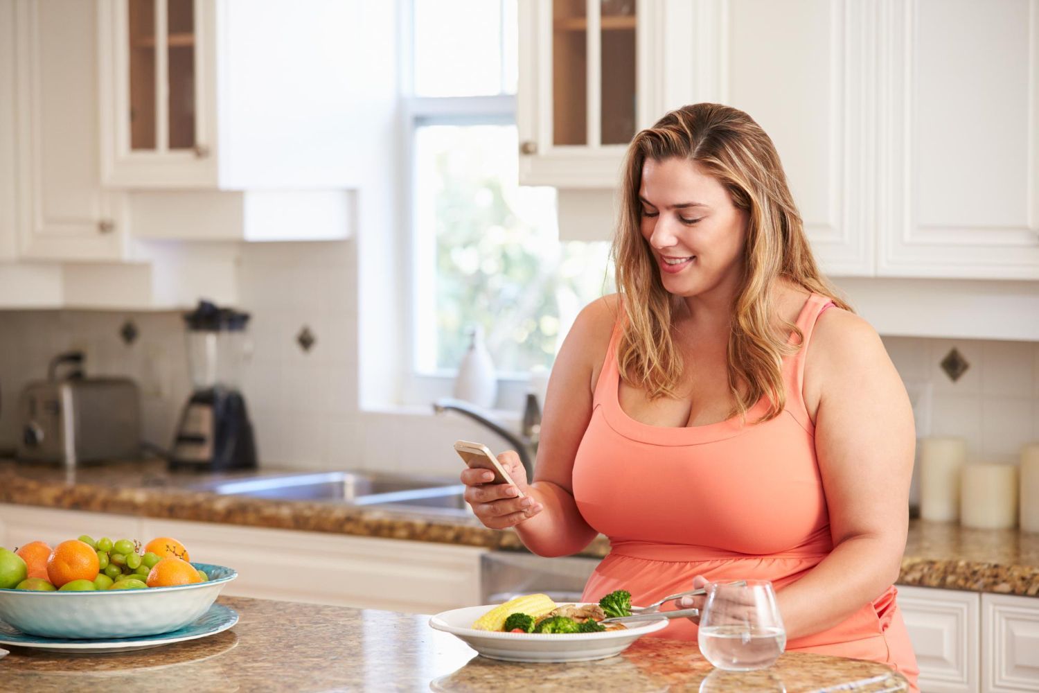 A woman is sitting at a kitchen counter looking at her cell phone.