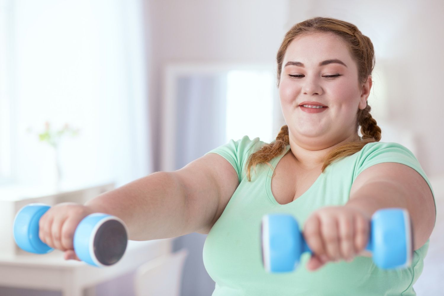 A woman is holding two blue dumbbells in her hands.