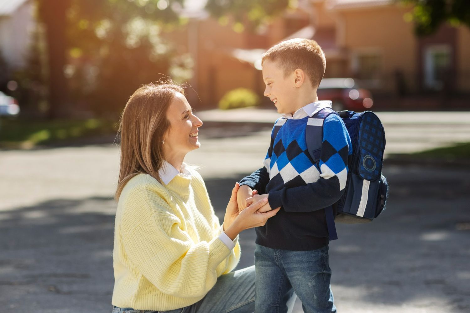 A woman is kneeling down next to a young boy with a backpack.