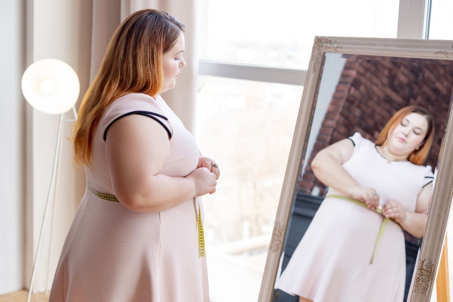 A woman is measuring her waist in front of a mirror.
