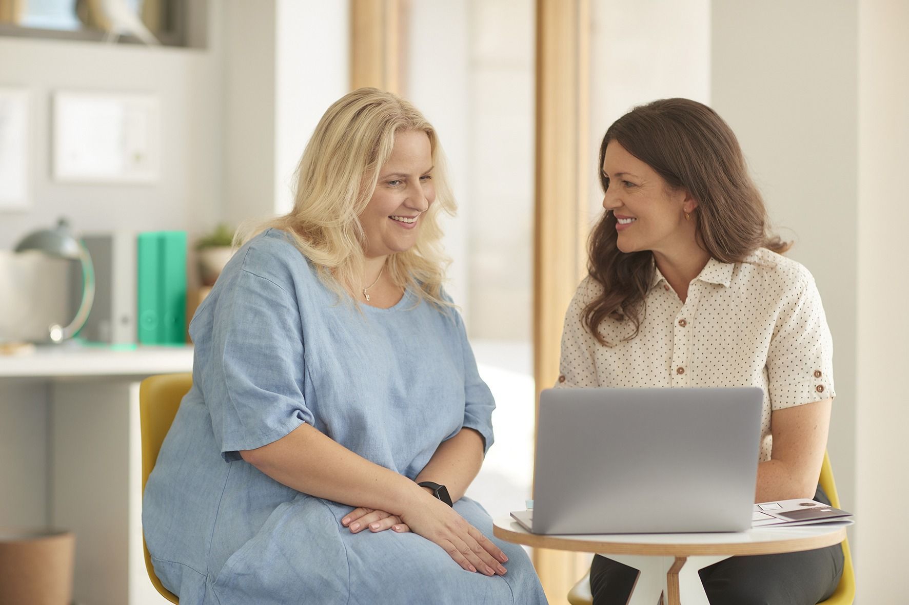 Two women are sitting at a table looking at a laptop computer.