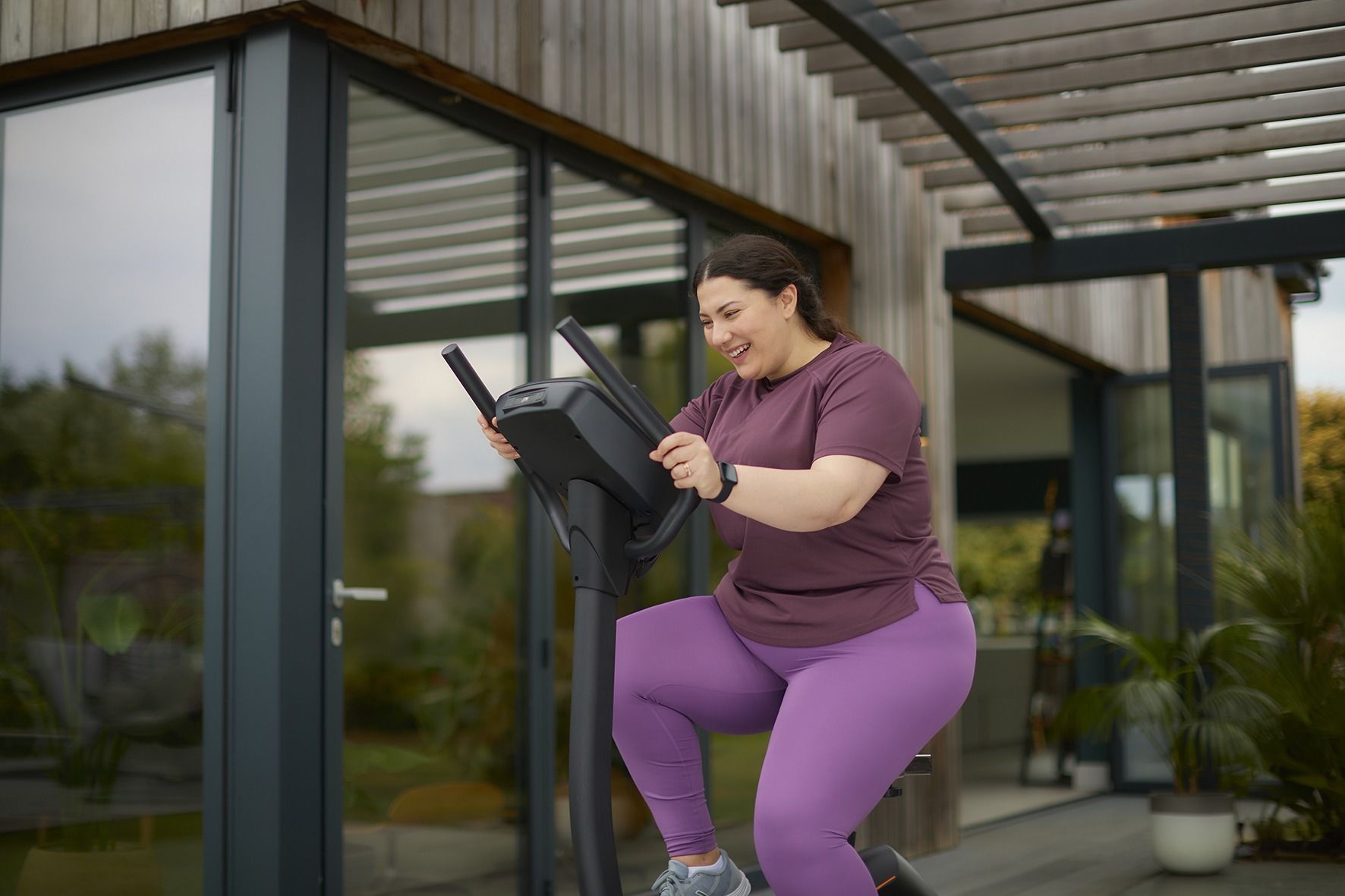 A woman is riding an exercise bike outside of a house.