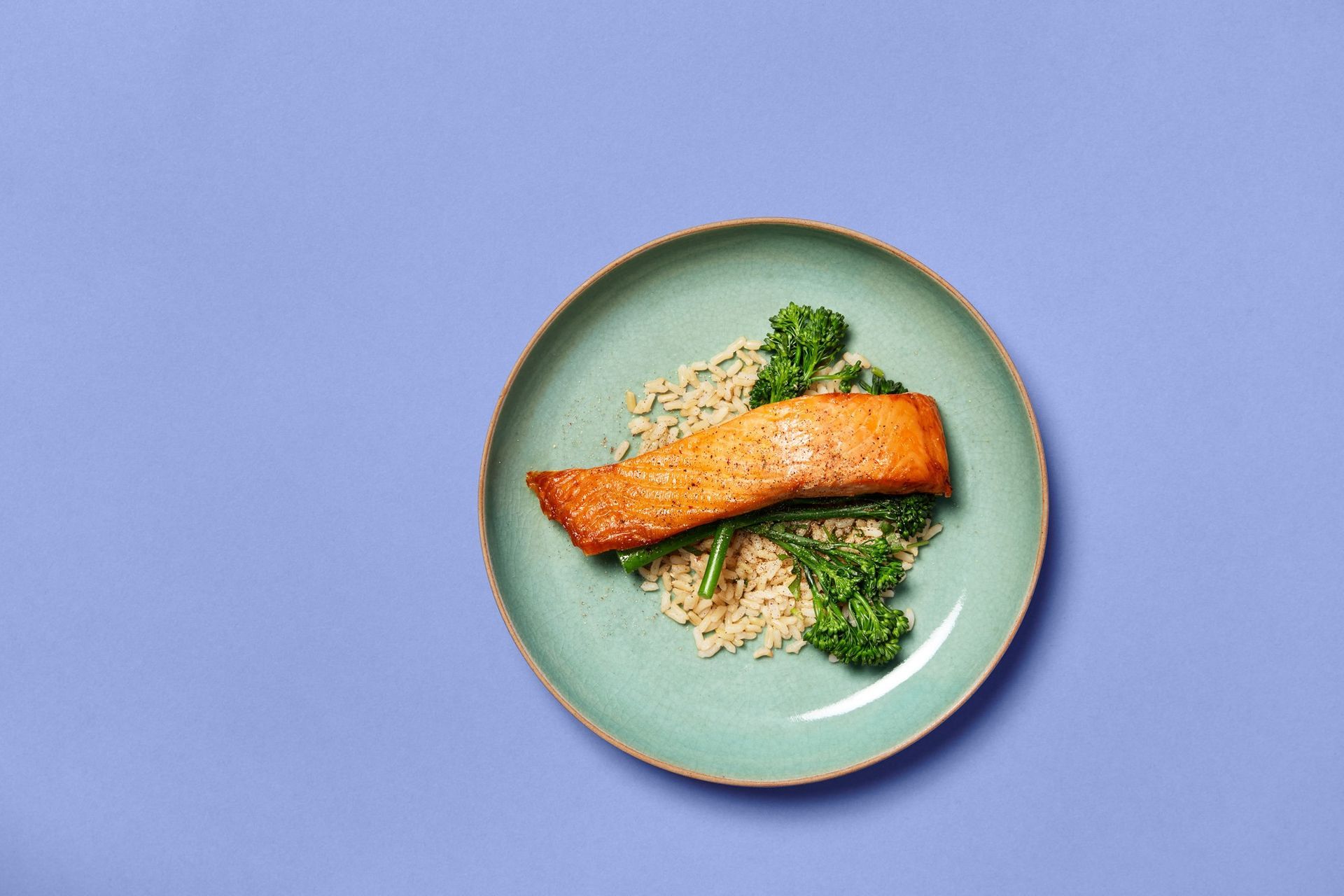 A plate of salmon with broccoli and rice on a blue background.