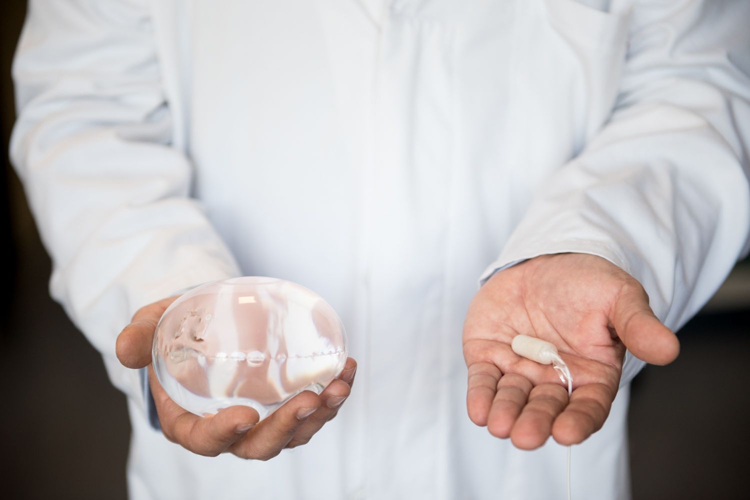 A man in a lab coat is holding two objects in his hands.