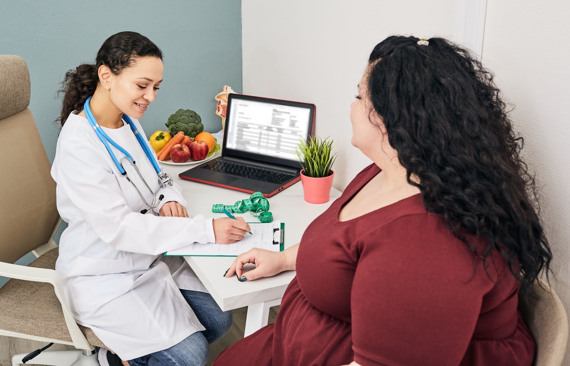 Doctor in white coat reviewing notes with patient at desk.