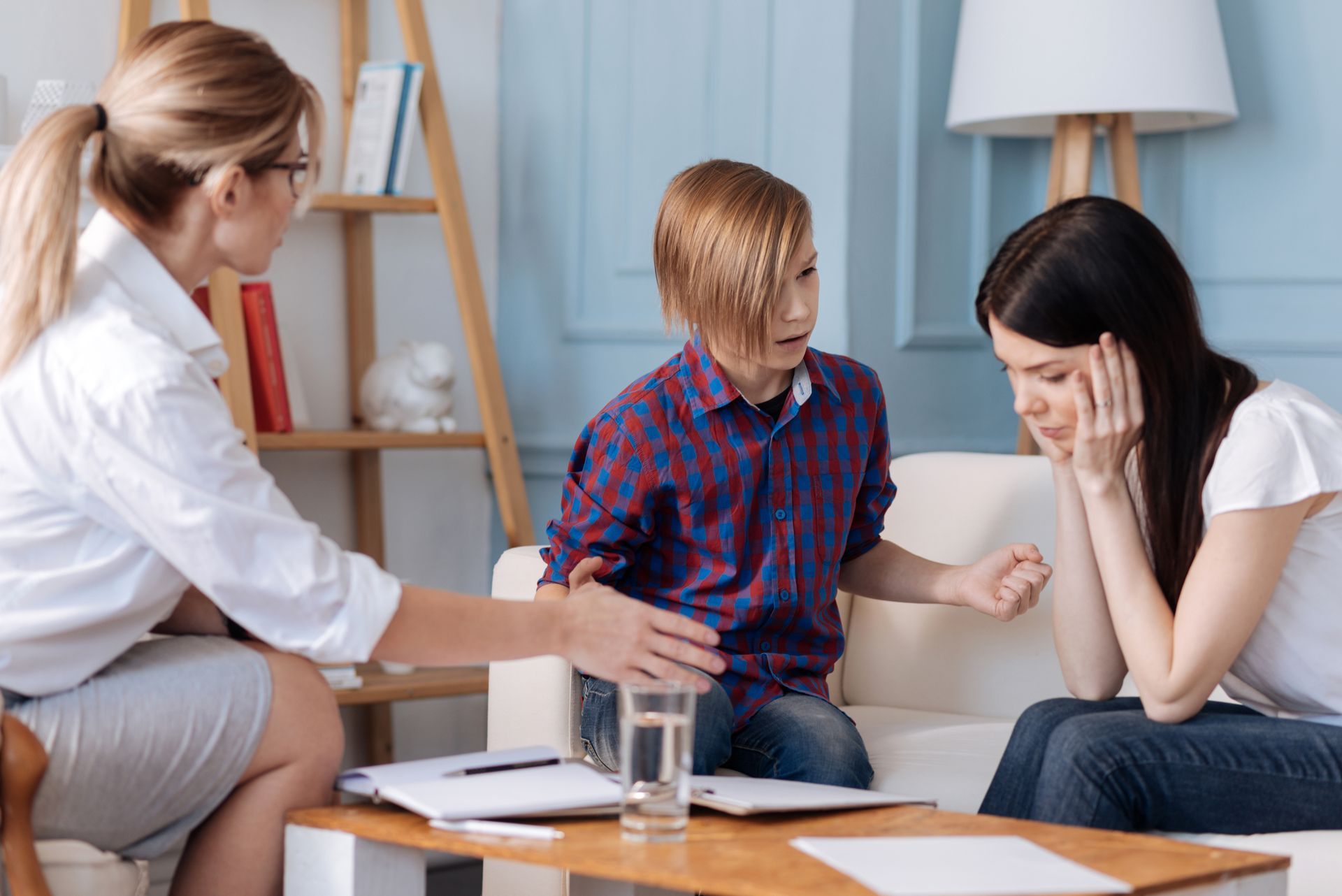 A woman is sitting on a couch talking to a boy and a girl.