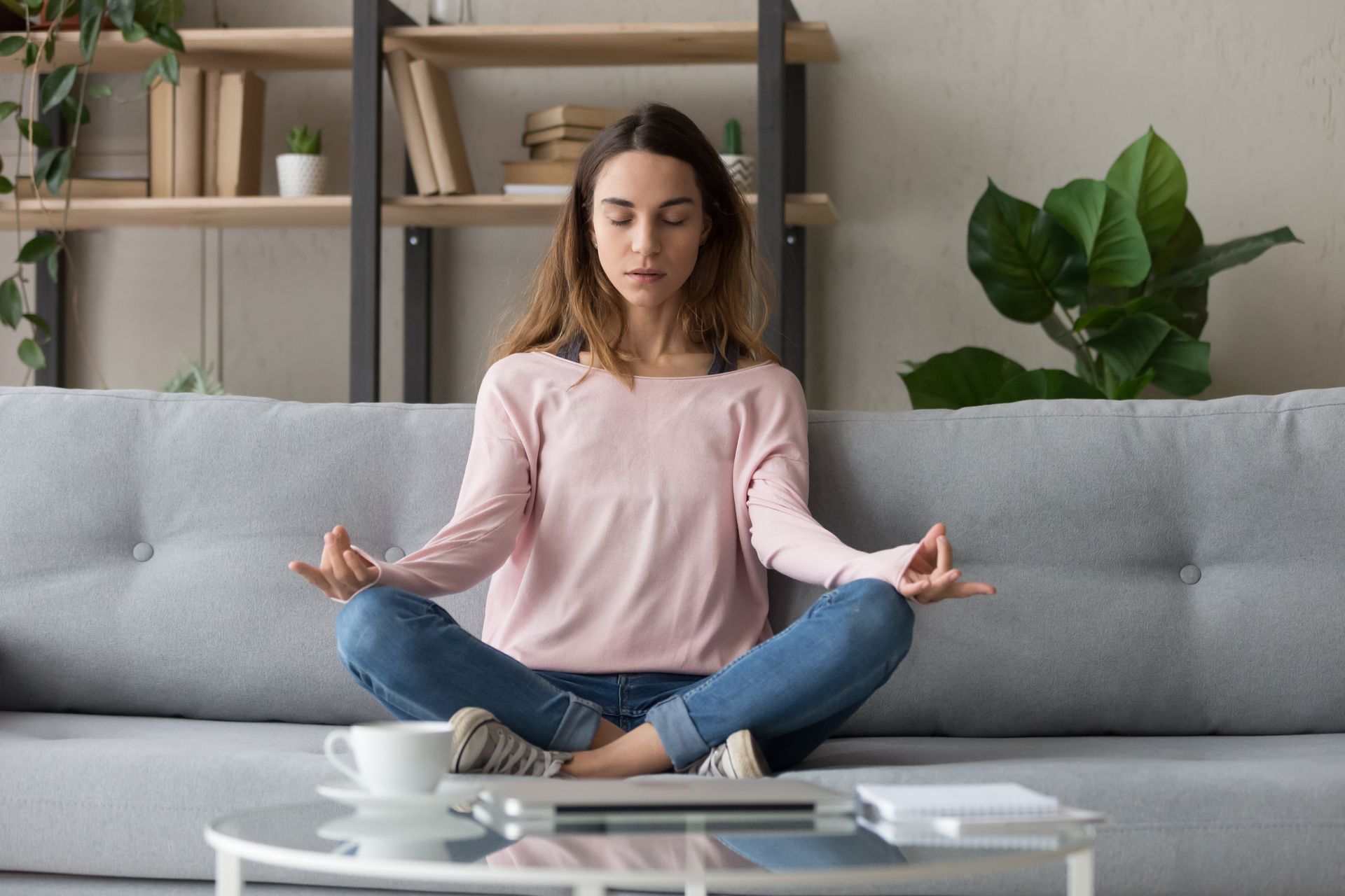 A woman is sitting on a couch meditating with her legs crossed.