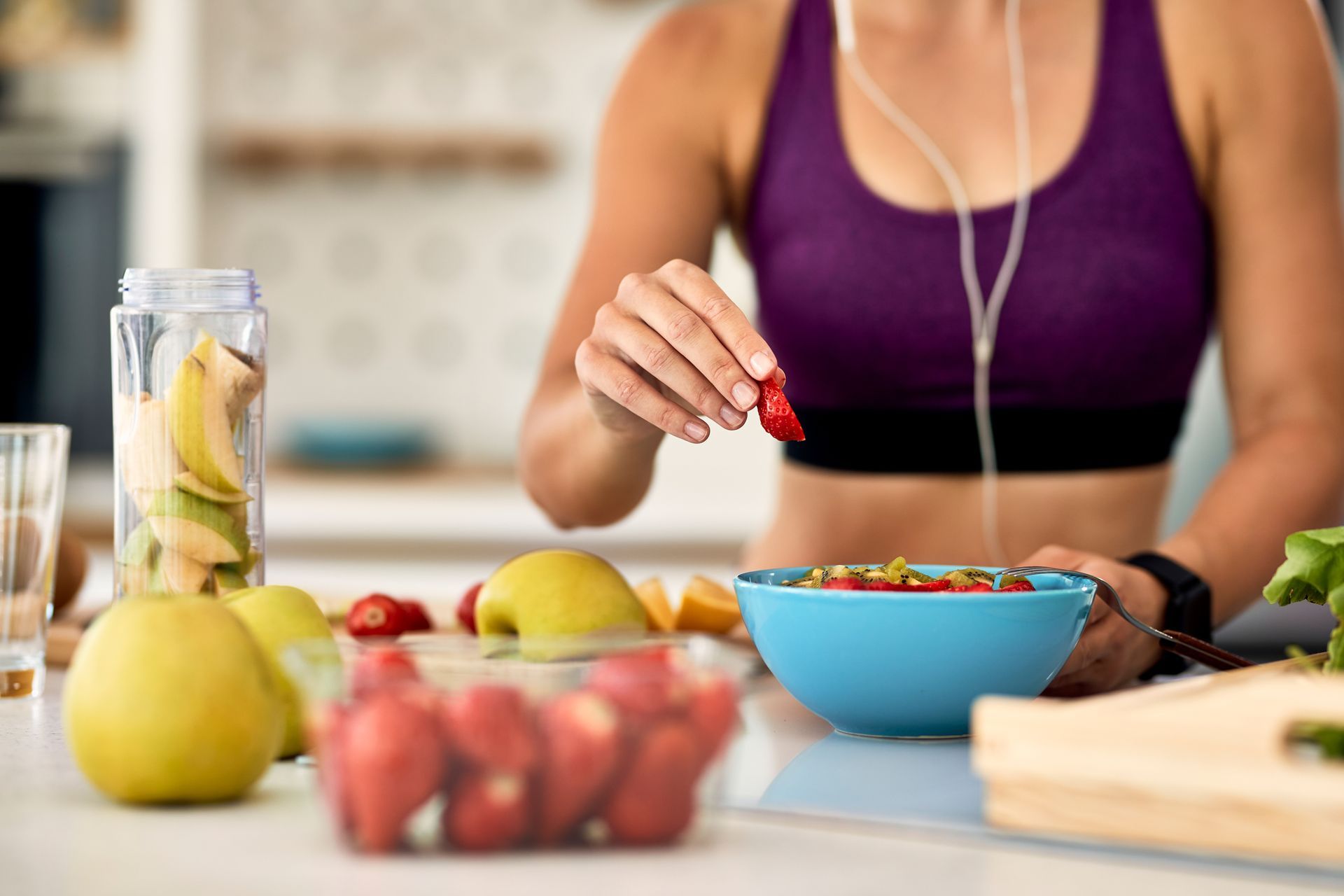 a woman is eating a bowl of fruit and cereal in a kitchen .