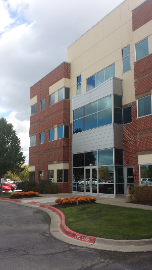 Red brick and beige office building with glass entrance and windows, under a cloudy sky.