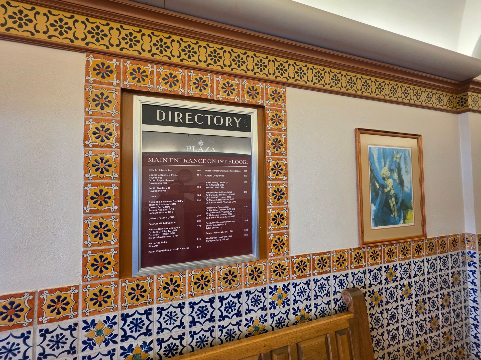 Wall with directory, bordered by floral tiles. A framed print hangs to the right.