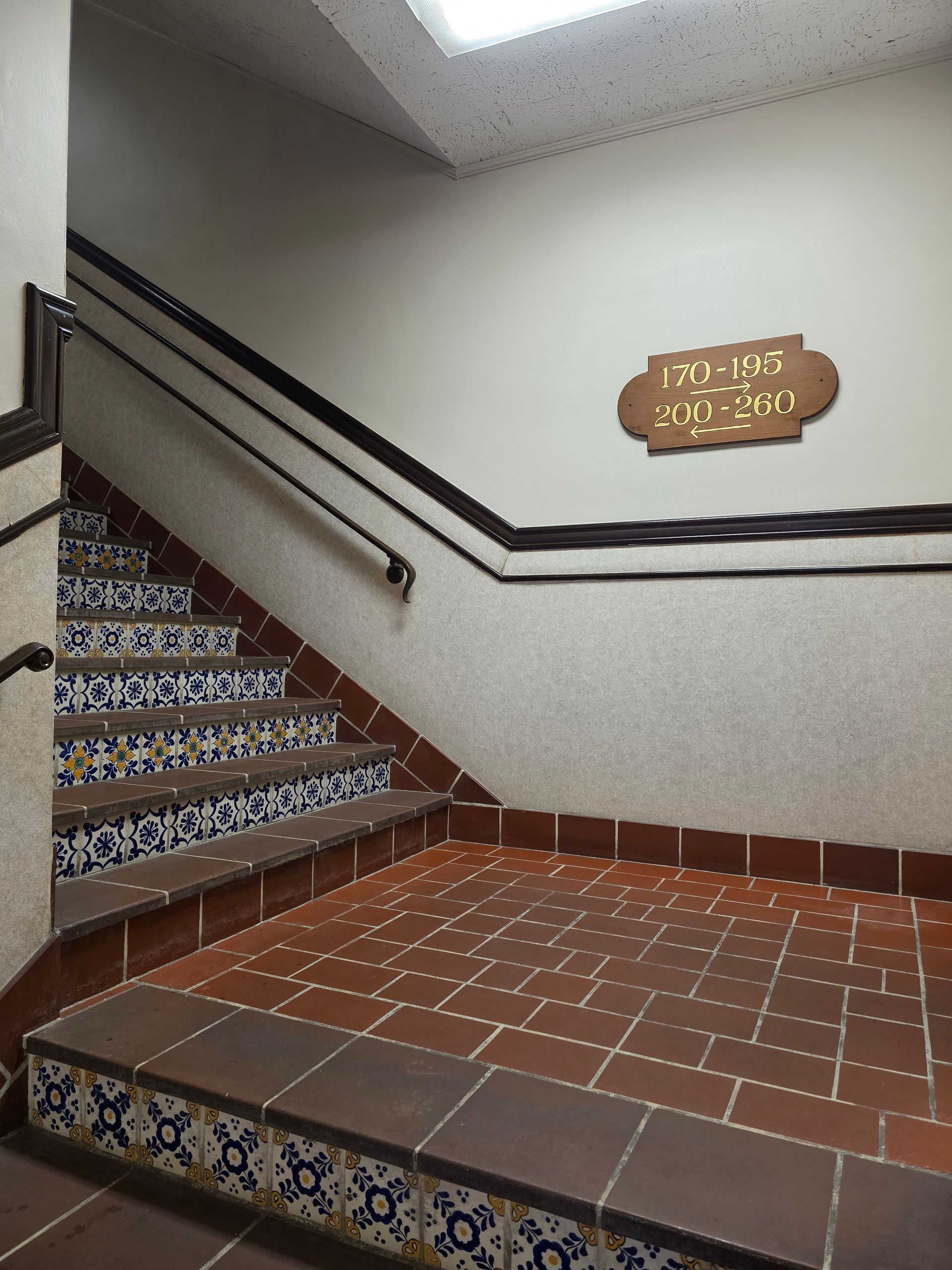 Stairwell with tiled steps and landing. Brown tile floor, blue and yellow patterned risers, dark handrails.