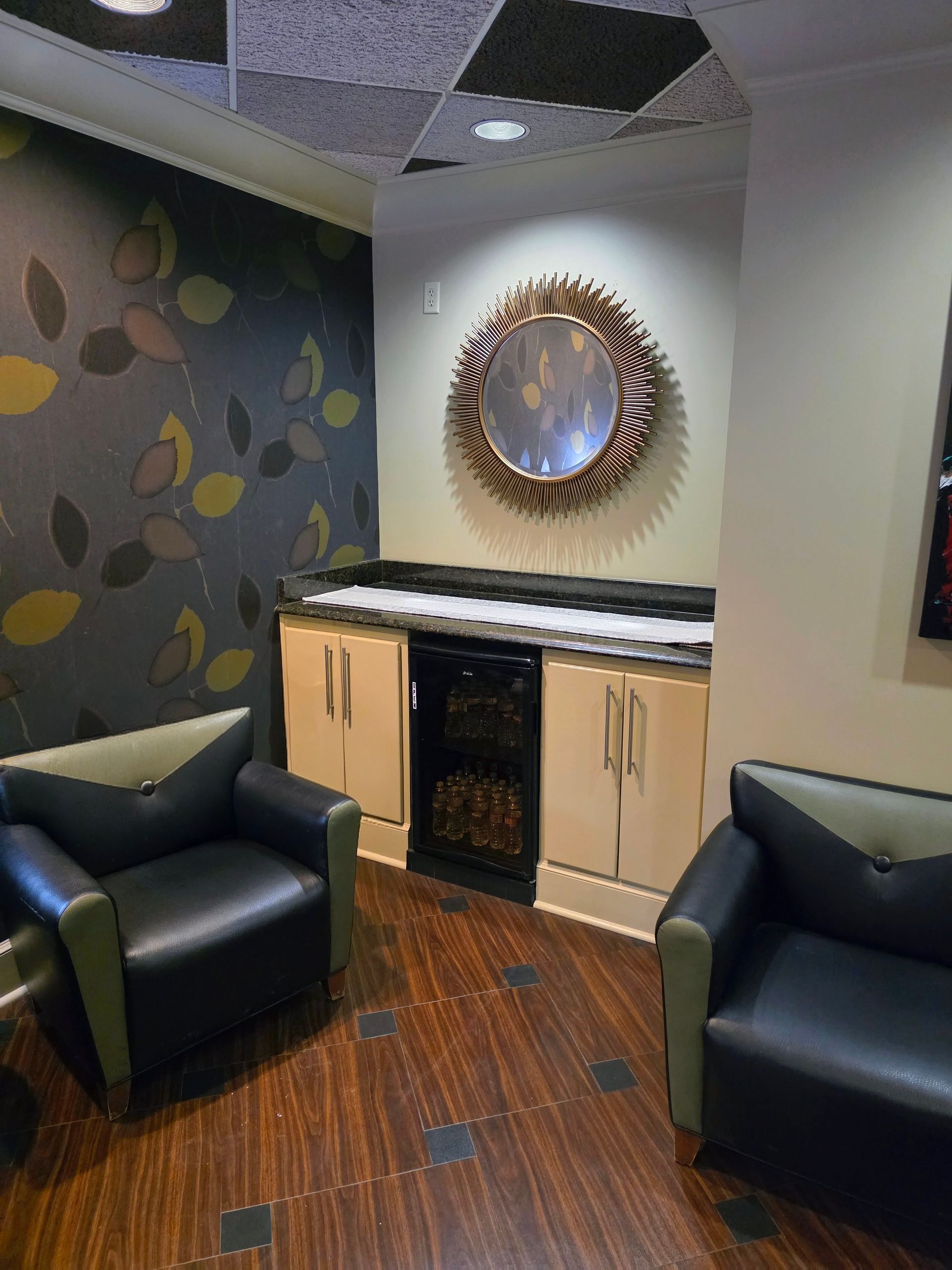Lounge area with black chairs, built-in bar, and ornate mirror on the wall, featuring leaf-patterned wallpaper.