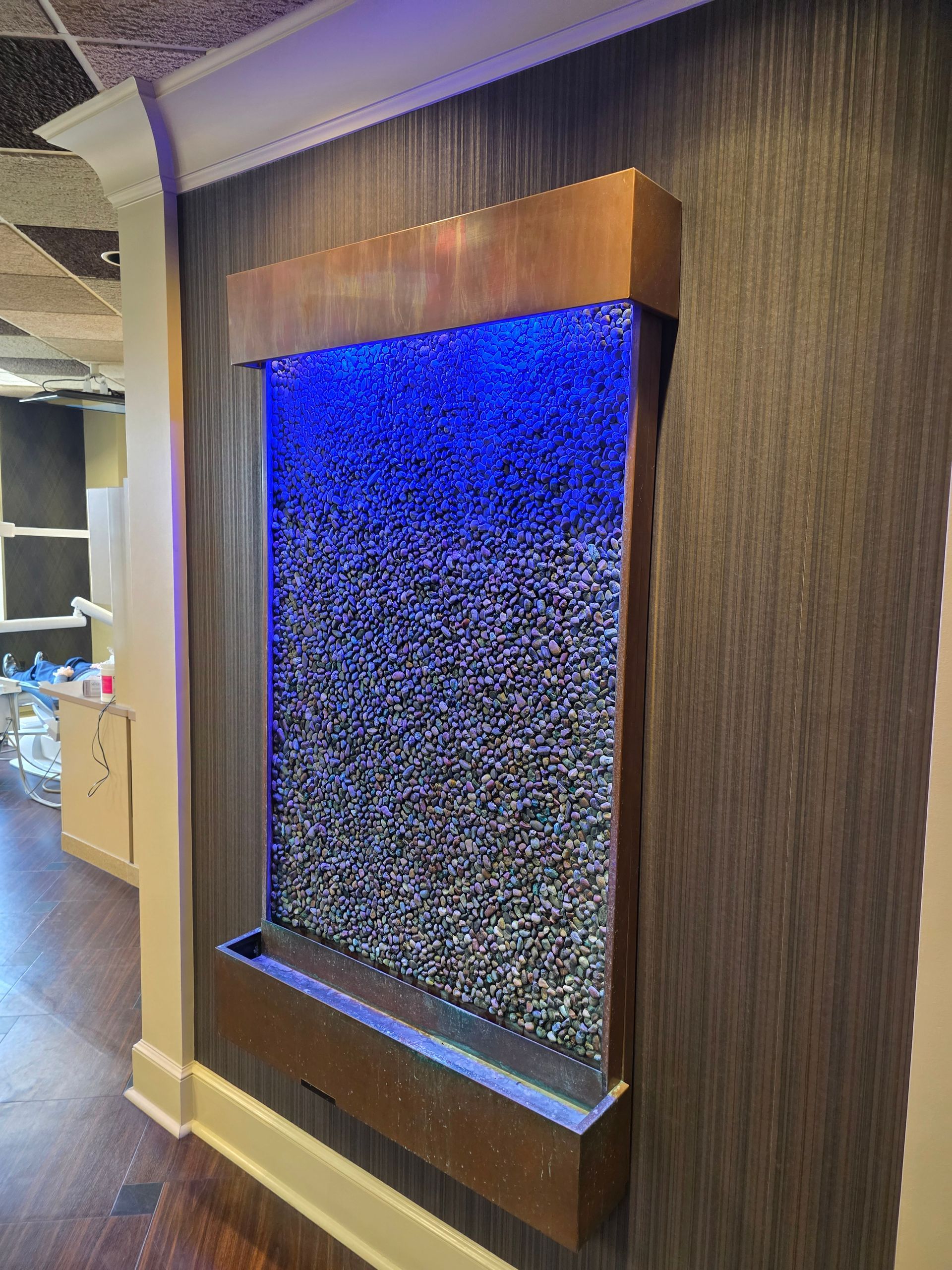 Wall fountain with copper trim and blue LED lighting, cascading water over textured glass.