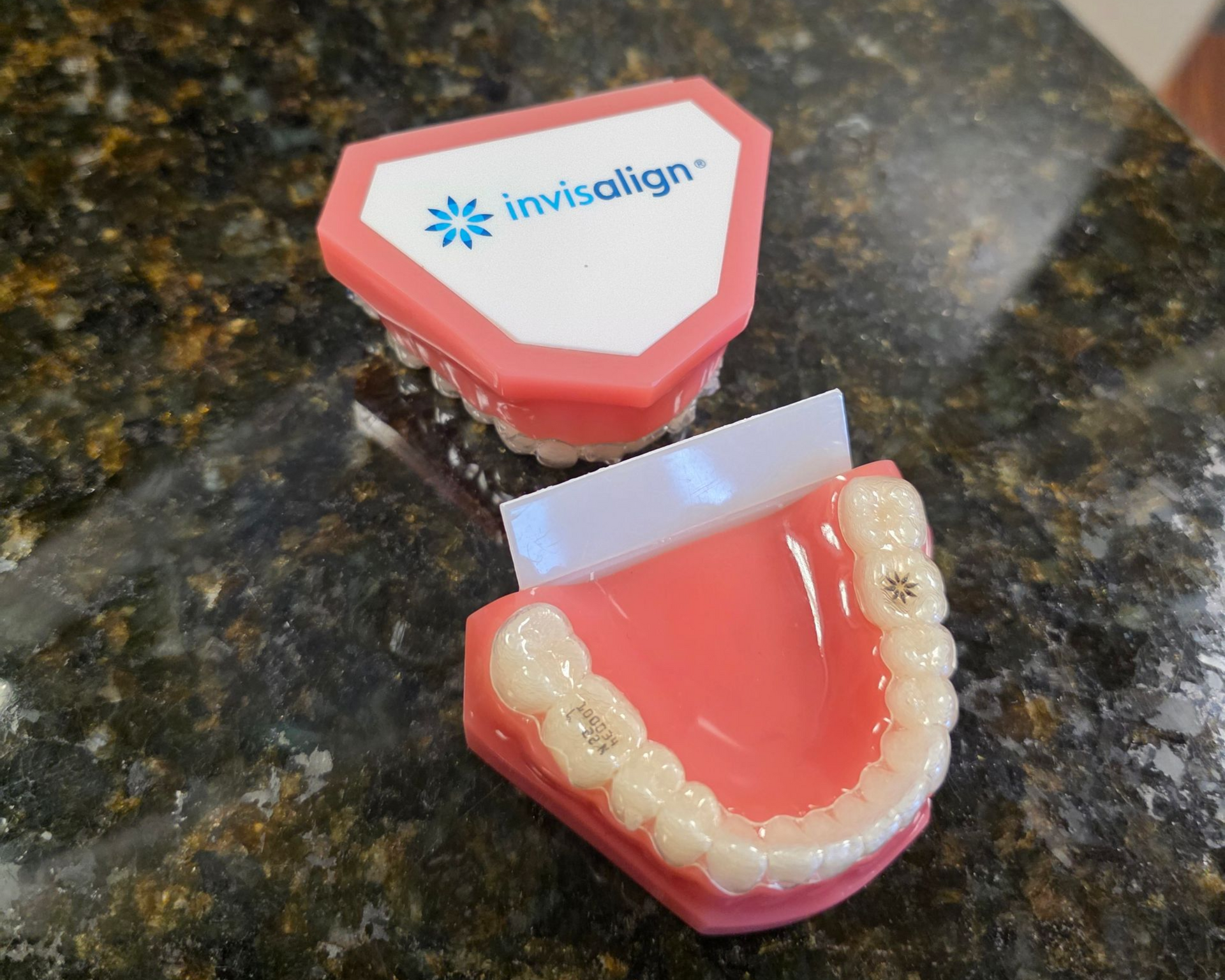 Two pink and white dental models with Invisalign logo on a speckled surface.