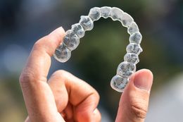 Hand holding clear, upper dental aligner, likely for teeth straightening.