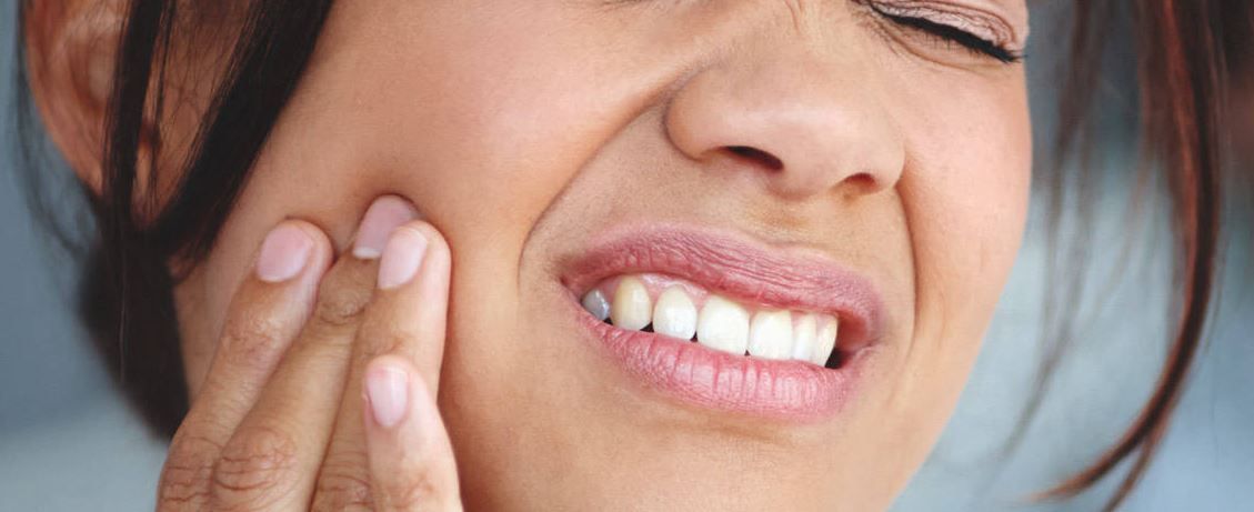 Woman with closed eyes, touching her cheek in pain, possibly due to a toothache.