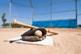 Baseball bat and glove with a ball on a home plate, set on a baseball field on a sunny day.