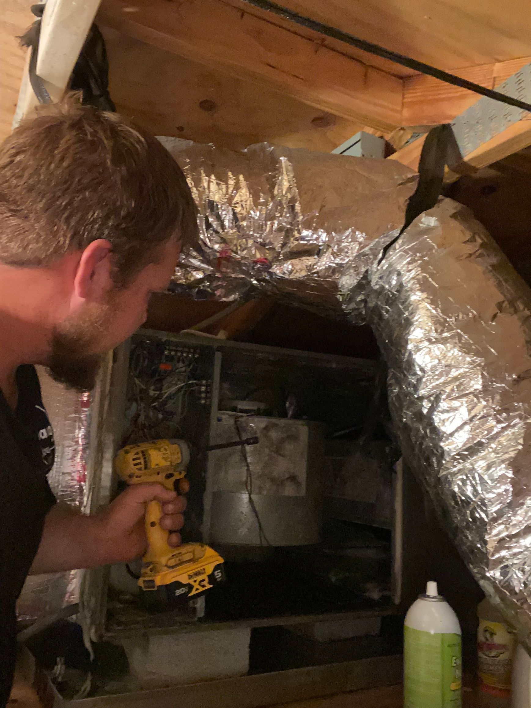 A man is using a drill to fix an air conditioner.