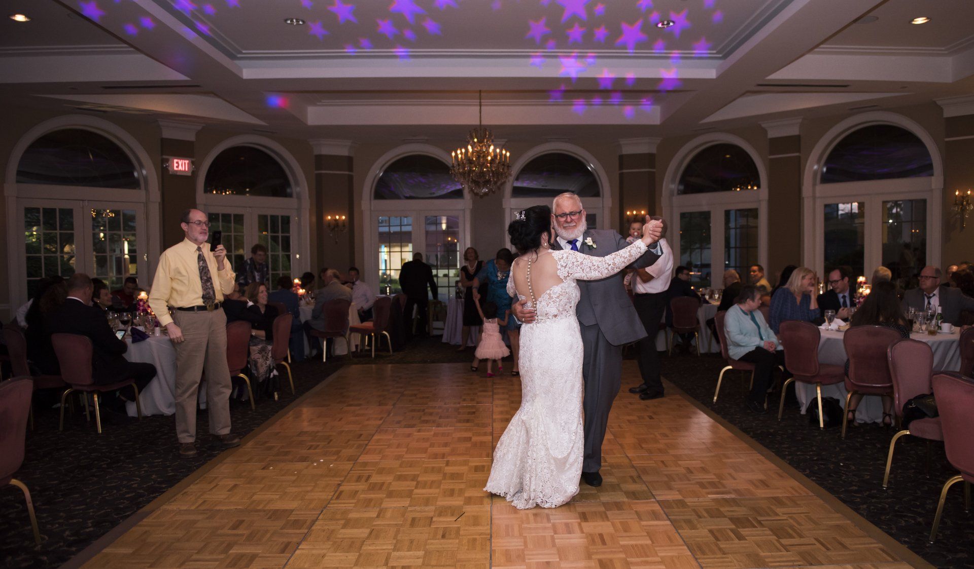 A bride and groom are dancing on a wooden dance floor at their wedding reception.