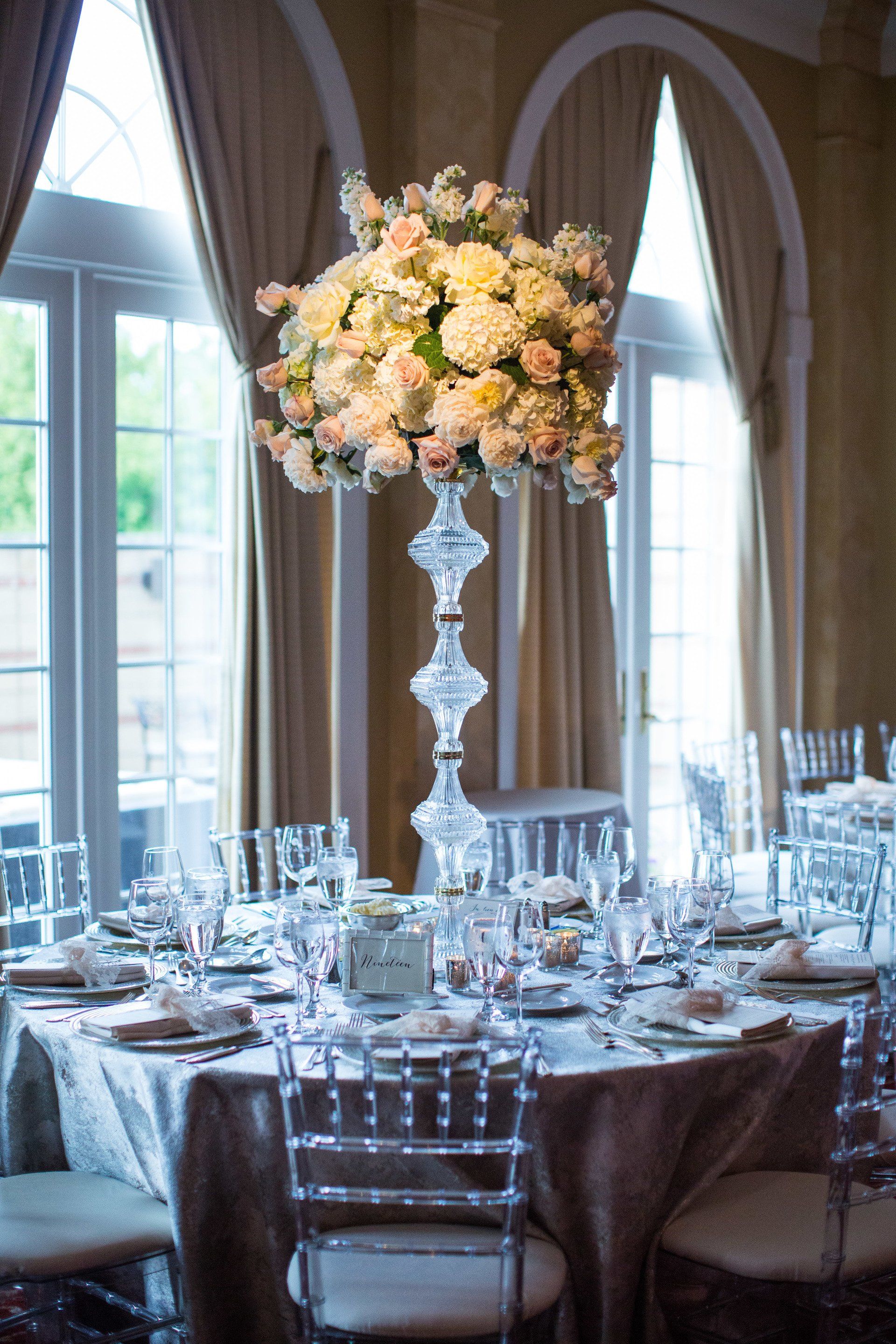 A table set for a wedding reception with a tall vase filled with flowers.