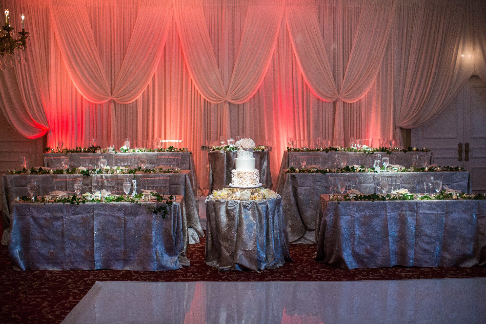 A wedding cake is sitting on top of a table in front of a pink curtain.